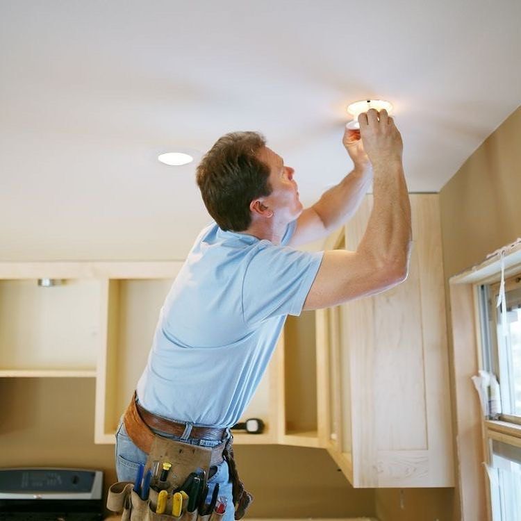 Electrician adjusting a ceiling light in a kitchen with wood cabinets
