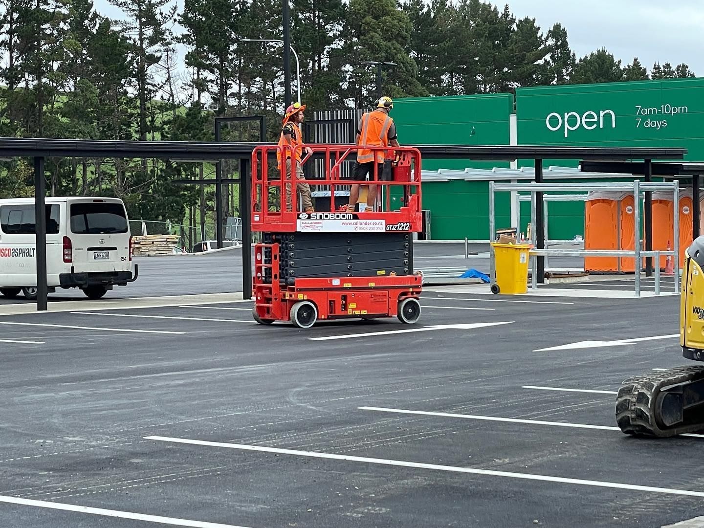 Workers in orange lifts at a parking lot outside a green store entrance