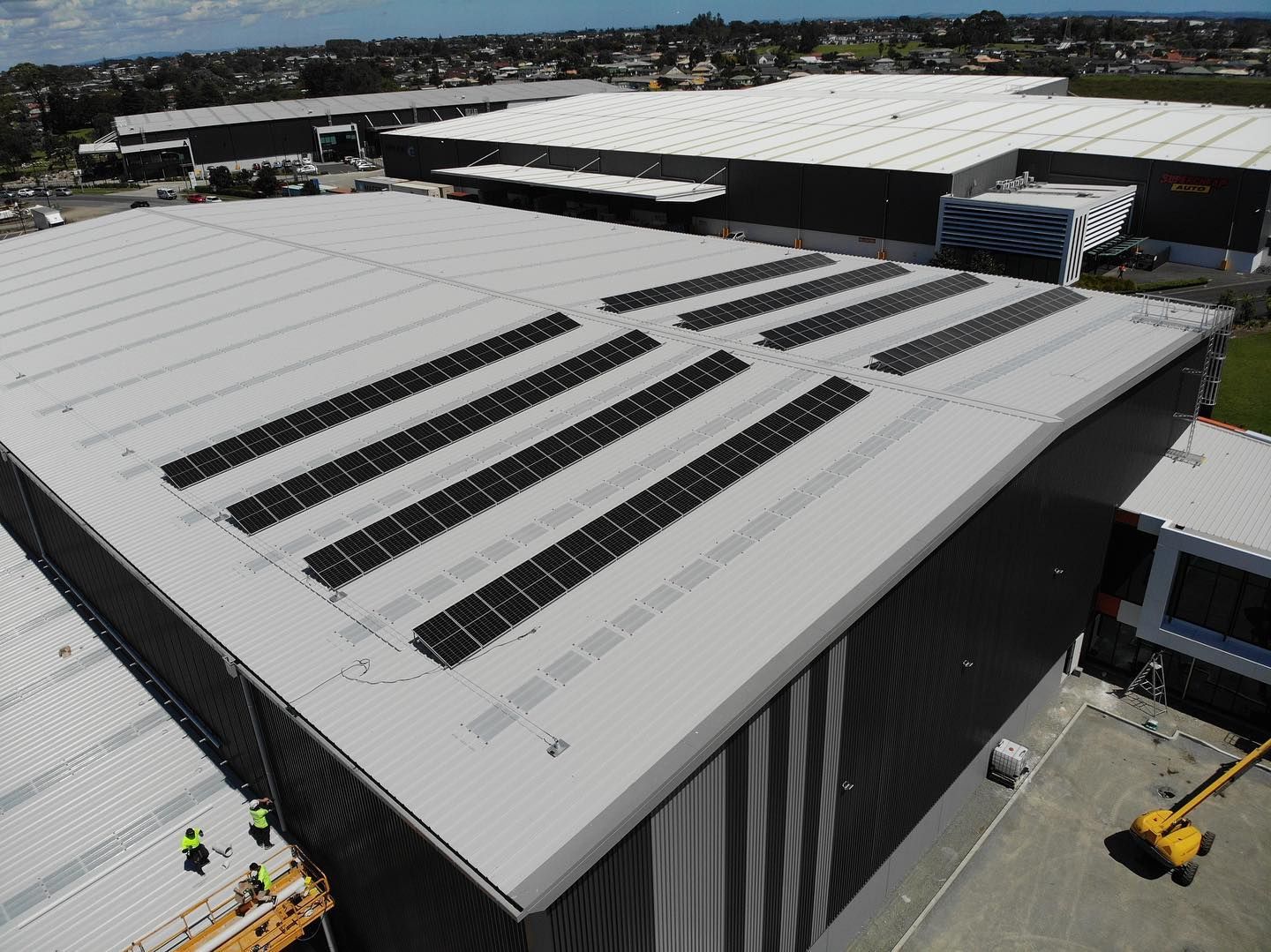 Aerial view of large industrial warehouses with gray roofs and rows of solar panels