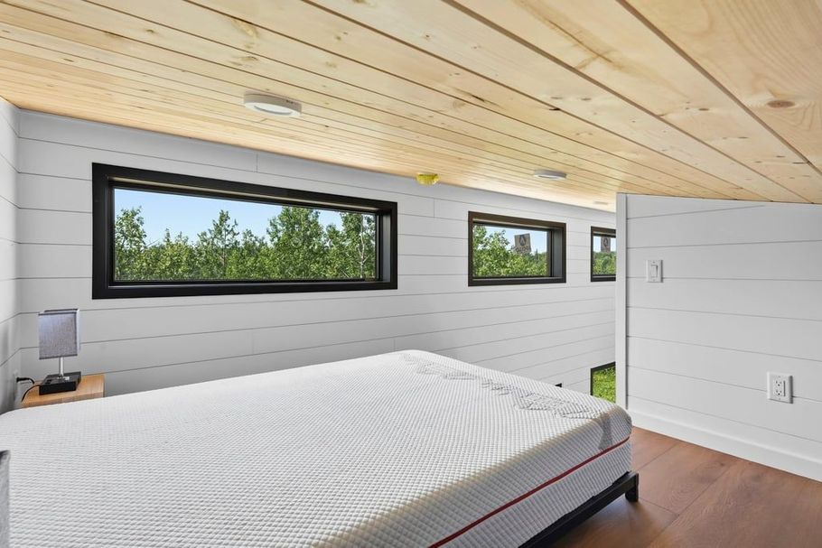 Modern bedroom with a white bed, wood ceiling, and narrow windows overlooking trees