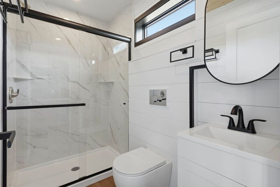 Modern bathroom with black-framed glass shower, white vanity, toilet, and round mirror