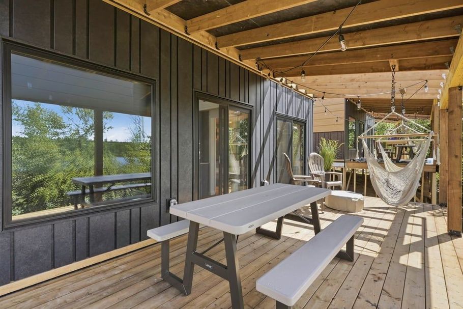 Covered porch with picnic table, bench, and hammock, overlooking trees through large windows.