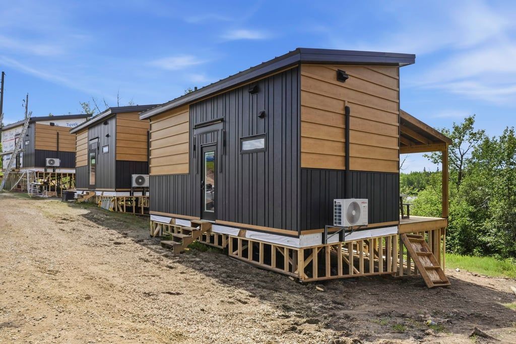 Row of modern tiny cabins with wood siding on a gravel lot under a clear sky
