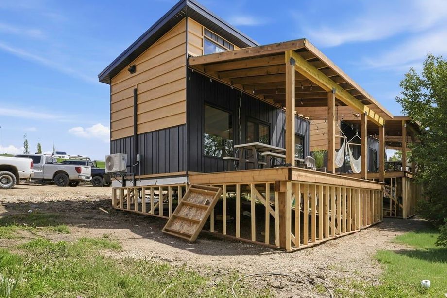 Wood-sided house under construction with a front porch and steps on a grassy lot
