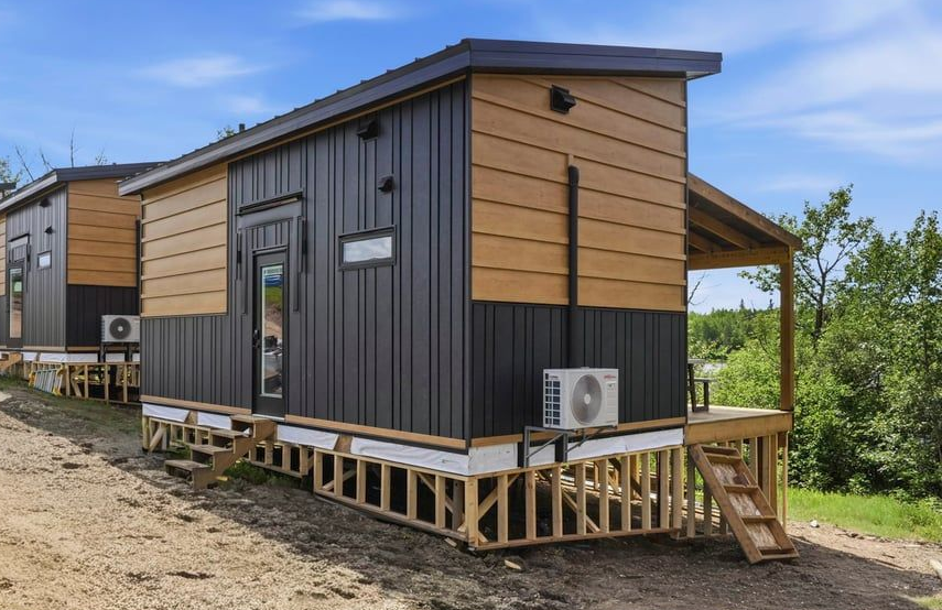 Modern tiny house with wood-and-black siding on a raised foundation in a rural setting