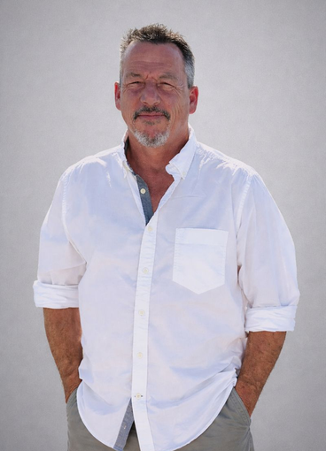 Man in a white button-up shirt with hands in pockets, standing against a plain light background.