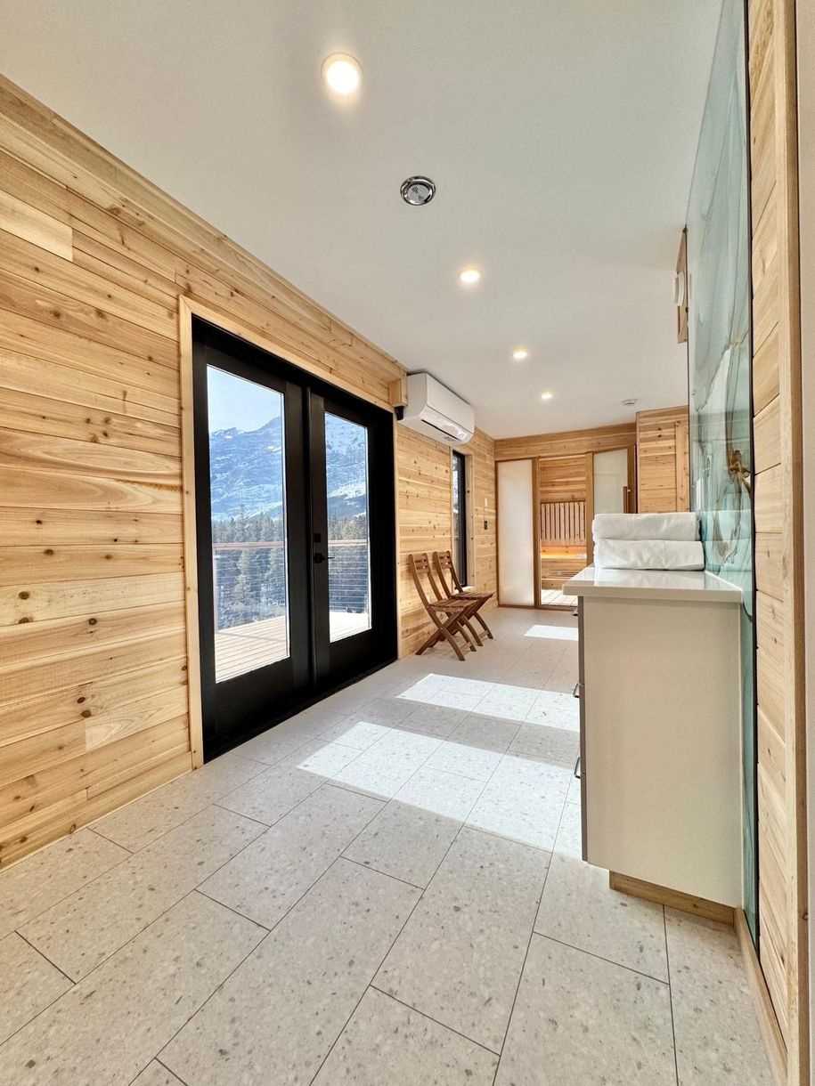 Bright hallway with wood-paneled walls, black-framed glass doors, and sunlight on white tile floor.