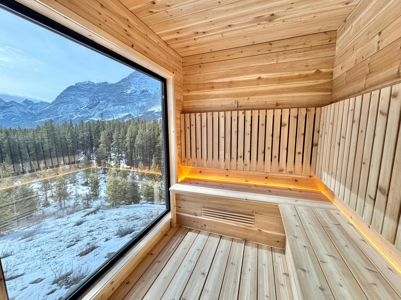 Wooden sauna interior with glowing bench and large window overlooking snowy mountains