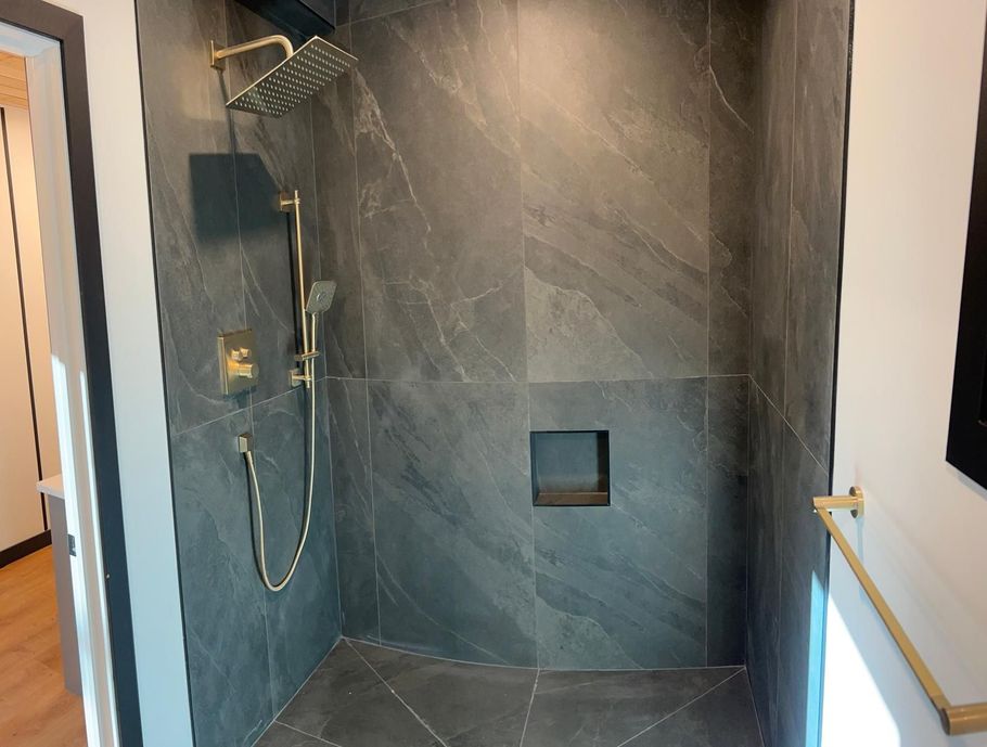 Modern walk-in shower with dark tile, rainfall showerhead, handheld sprayer, and built-in niche.