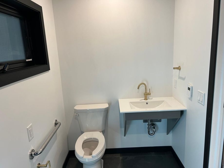 Accessible bathroom with toilet, wall-mounted sink, grab bars, and a mirror.