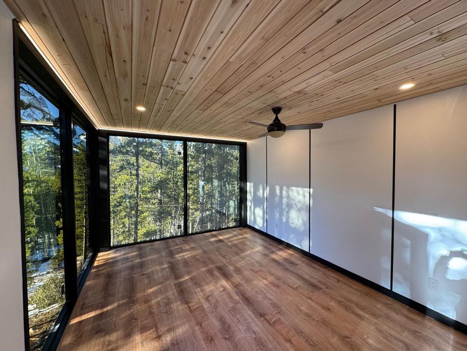 Empty modern room with wood ceiling, large windows, and ceiling fan overlooking trees