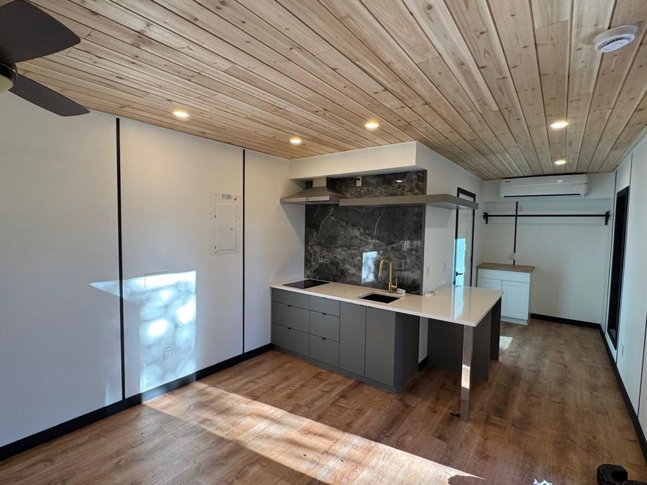 Compact kitchen with white walls, wood ceiling, gray cabinets, and sunlight on wood flooring