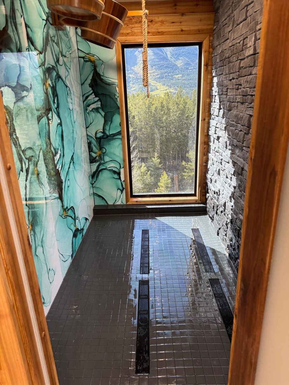 Narrow indoor shower with stone walls, dark tile floor, and a large window overlooking trees and mountains