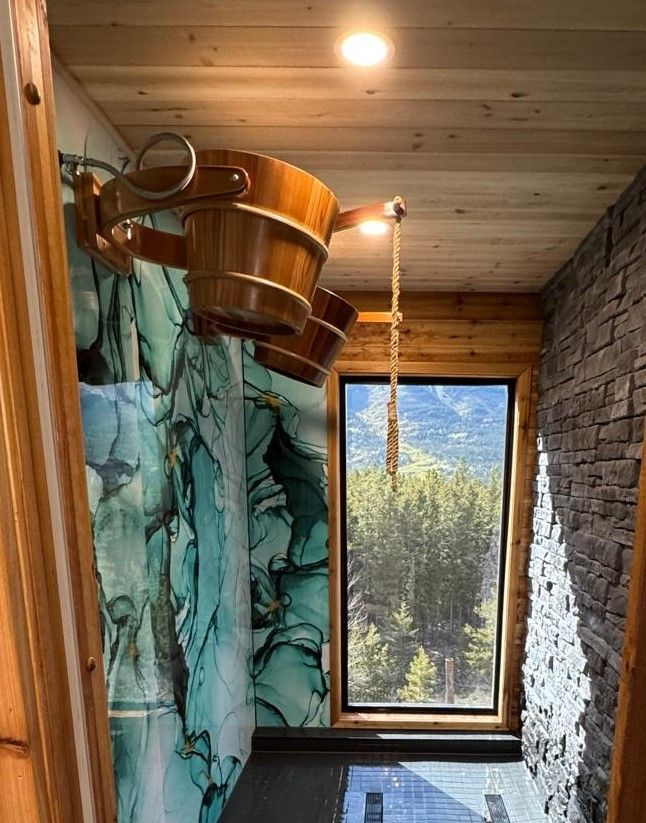 Rustic shower with turquoise curtain, wooden tub, stone wall, and a tall window overlooking trees and mountains