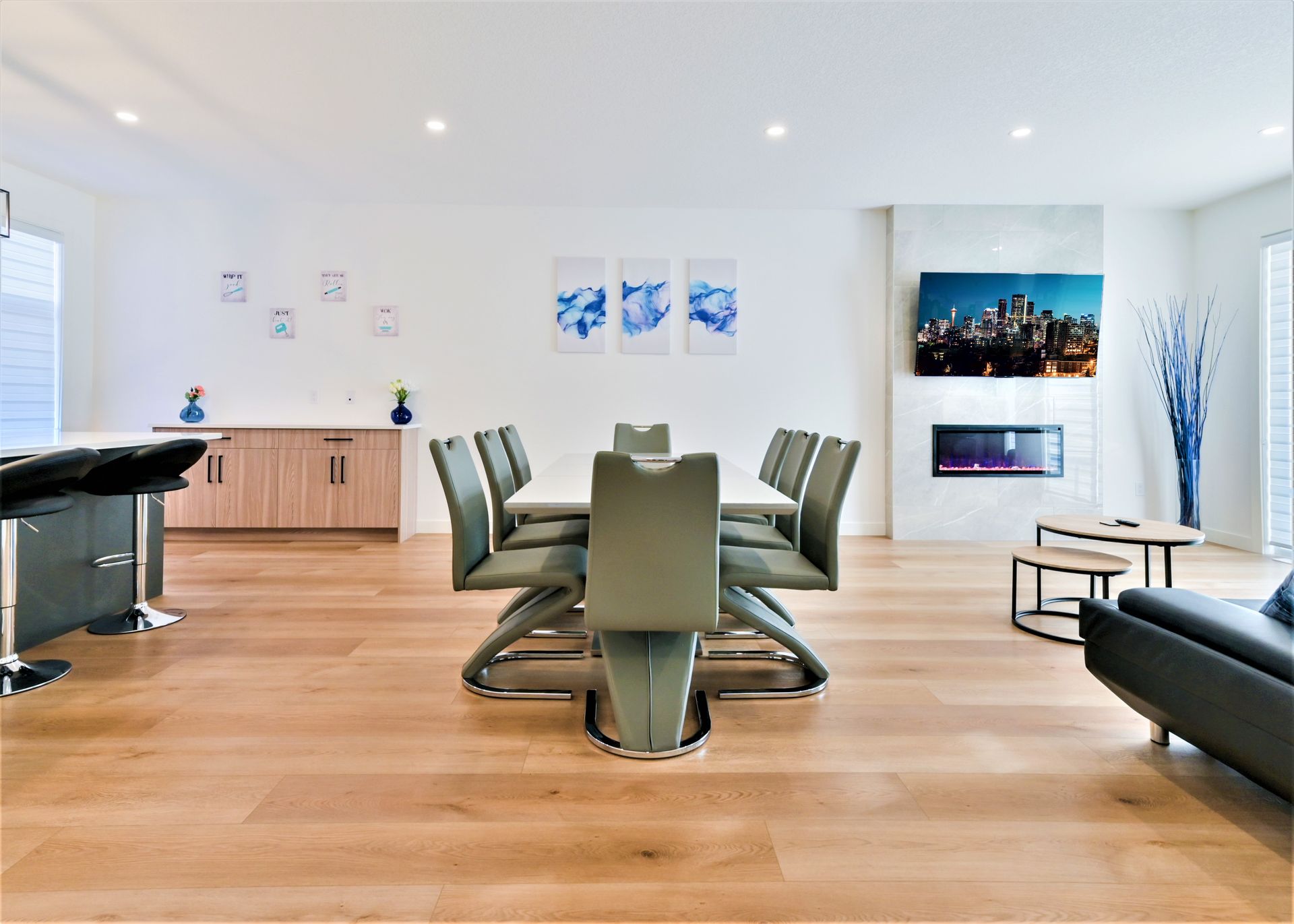 Modern conference room with wood floors, long table, black chairs, wall art, and a lounge area with a TV