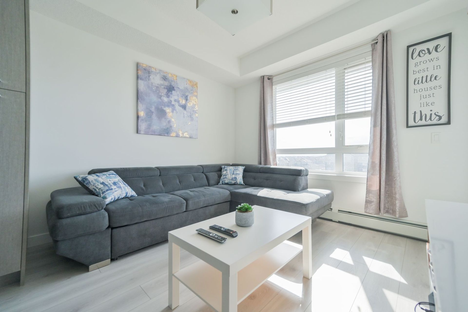 Bright living room with gray sectional, white coffee table, large window, and wall art