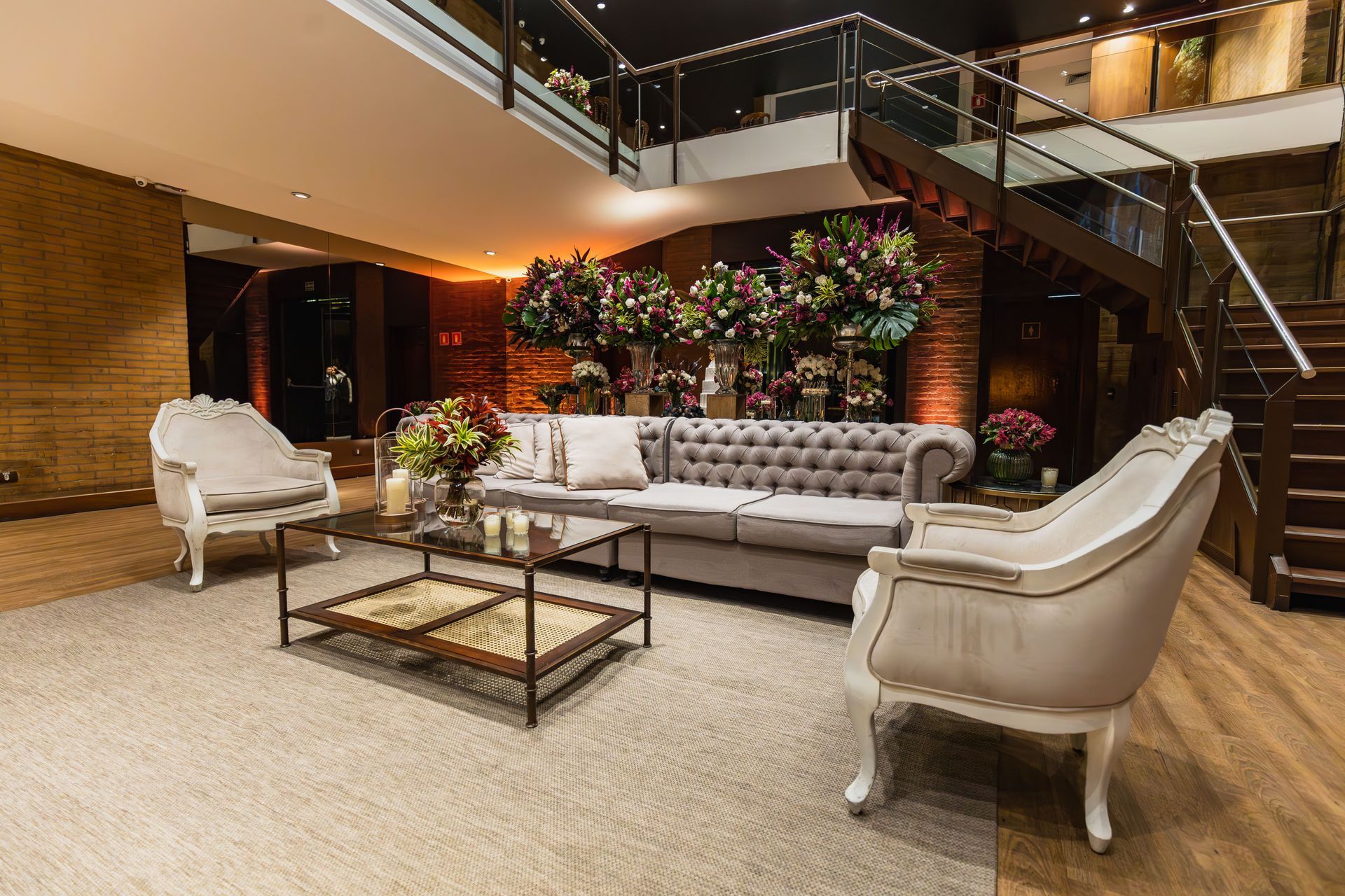 Elegant hotel lobby with beige seating, glass coffee table, and staircase amid warm lighting and greenery