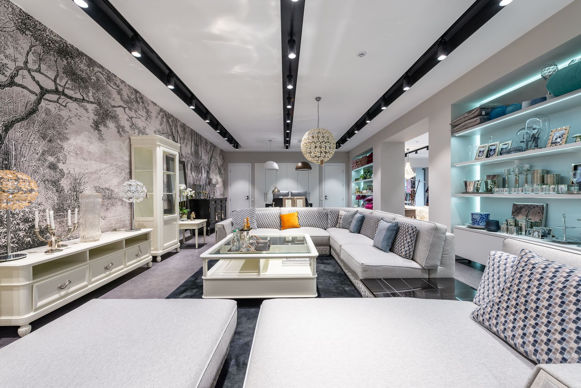 Modern showroom living room with white sofas, glass tables, black-and-white decor, and teal shelving