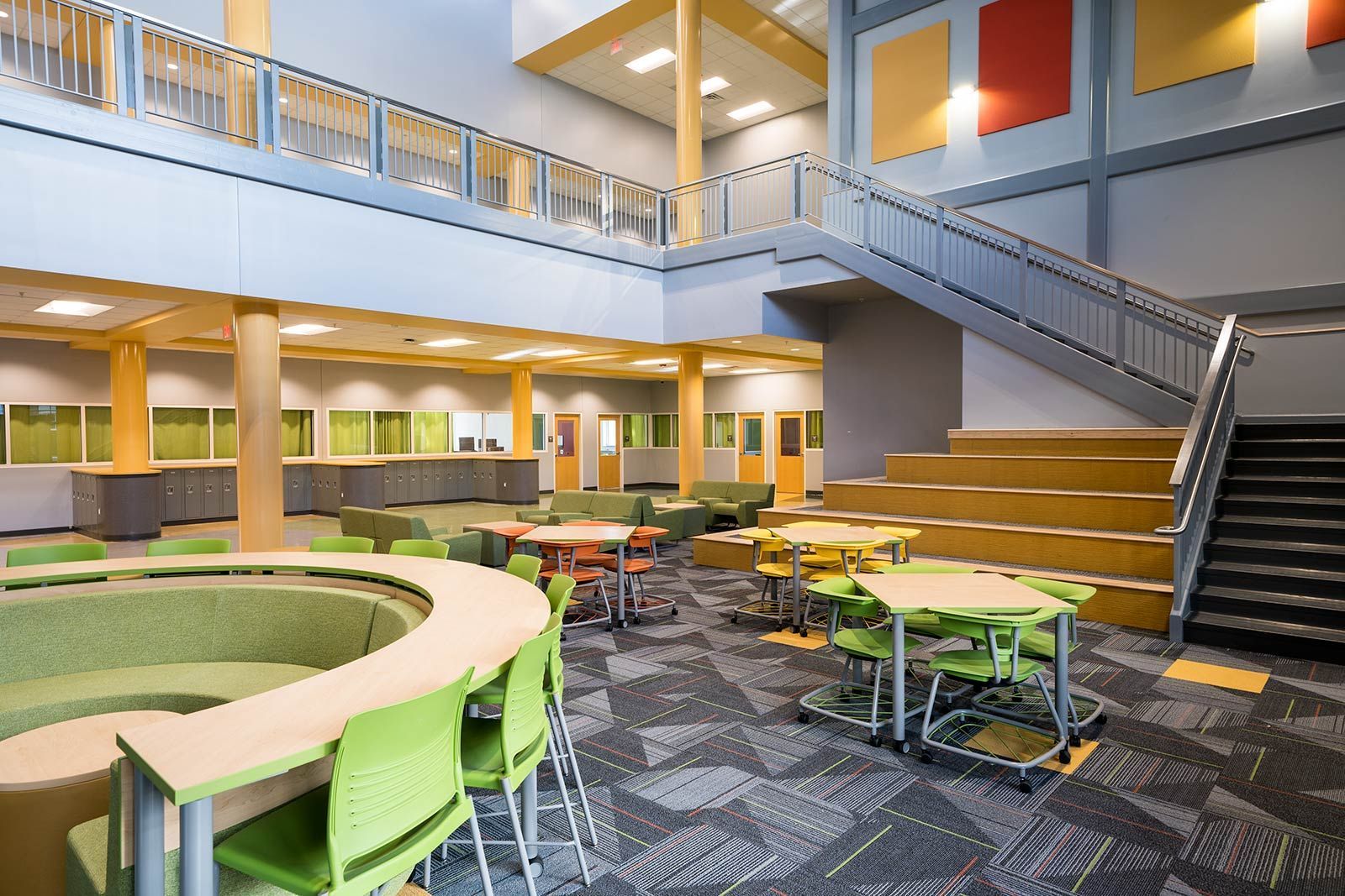 Modern lobby with circular seating, tables, staircase, and upper-level balconies in bright colors