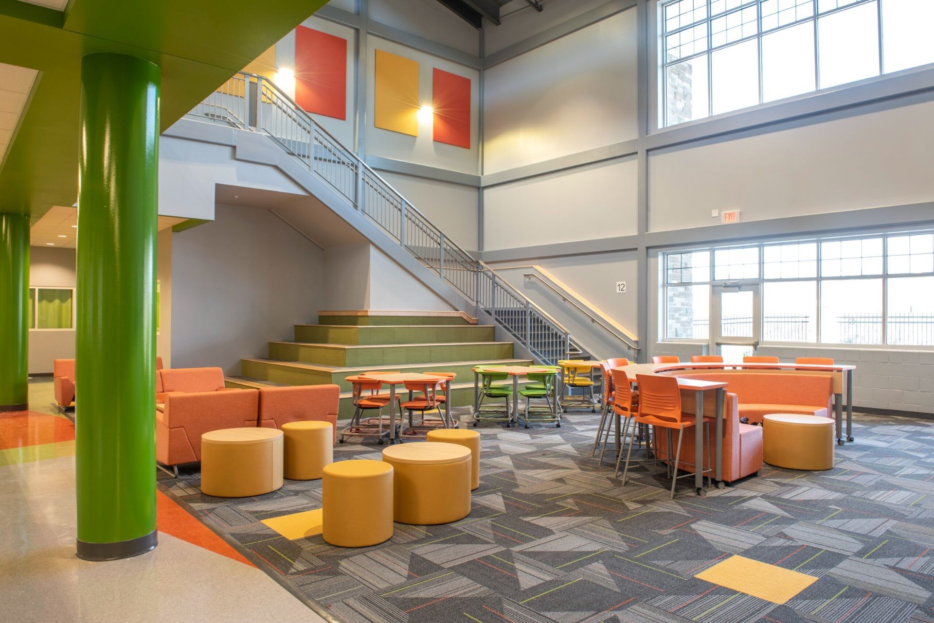 Modern lobby with green columns, orange seating, staircase, and bright windows