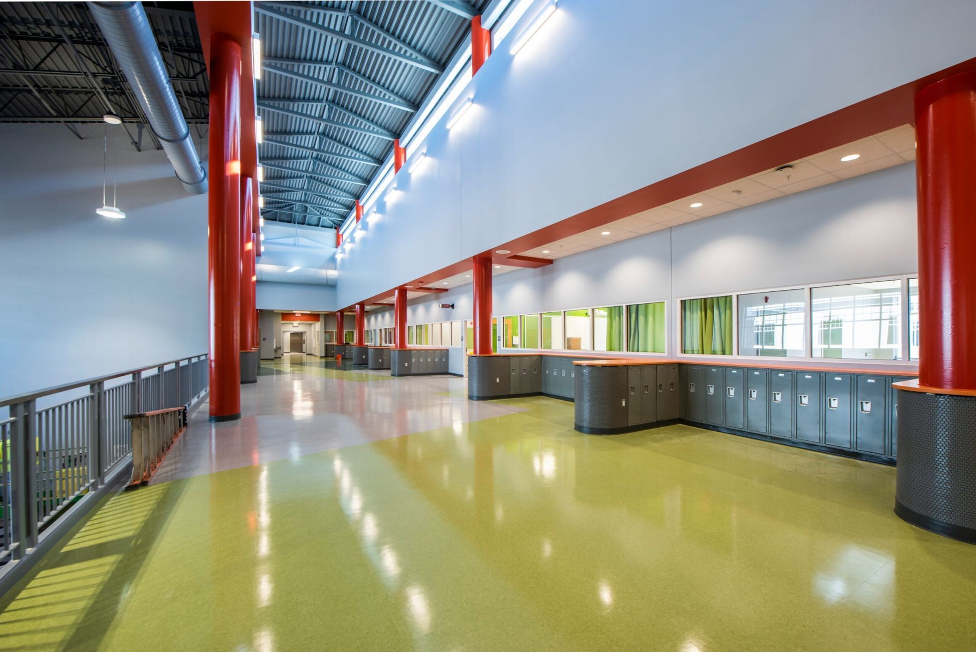 Empty school hallway with bright yellow floor, red columns, windows, and blue lockers.