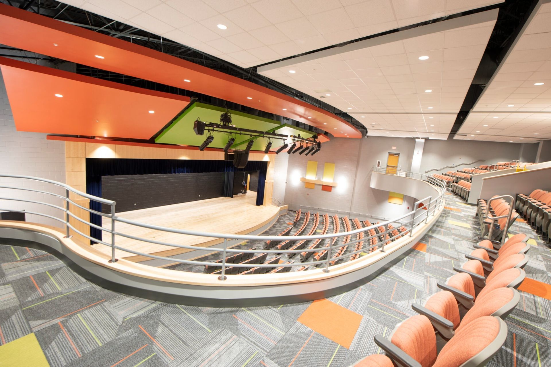 Empty modern auditorium with curved rows of orange seats and a stage under orange and green accents