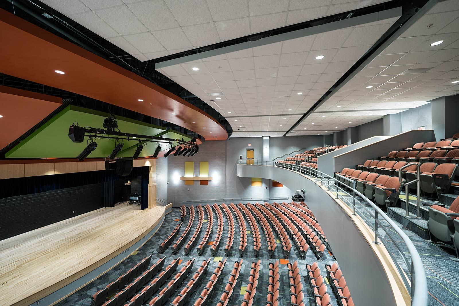 Modern auditorium with rows of red seats, stage lighting, and a curved balcony view