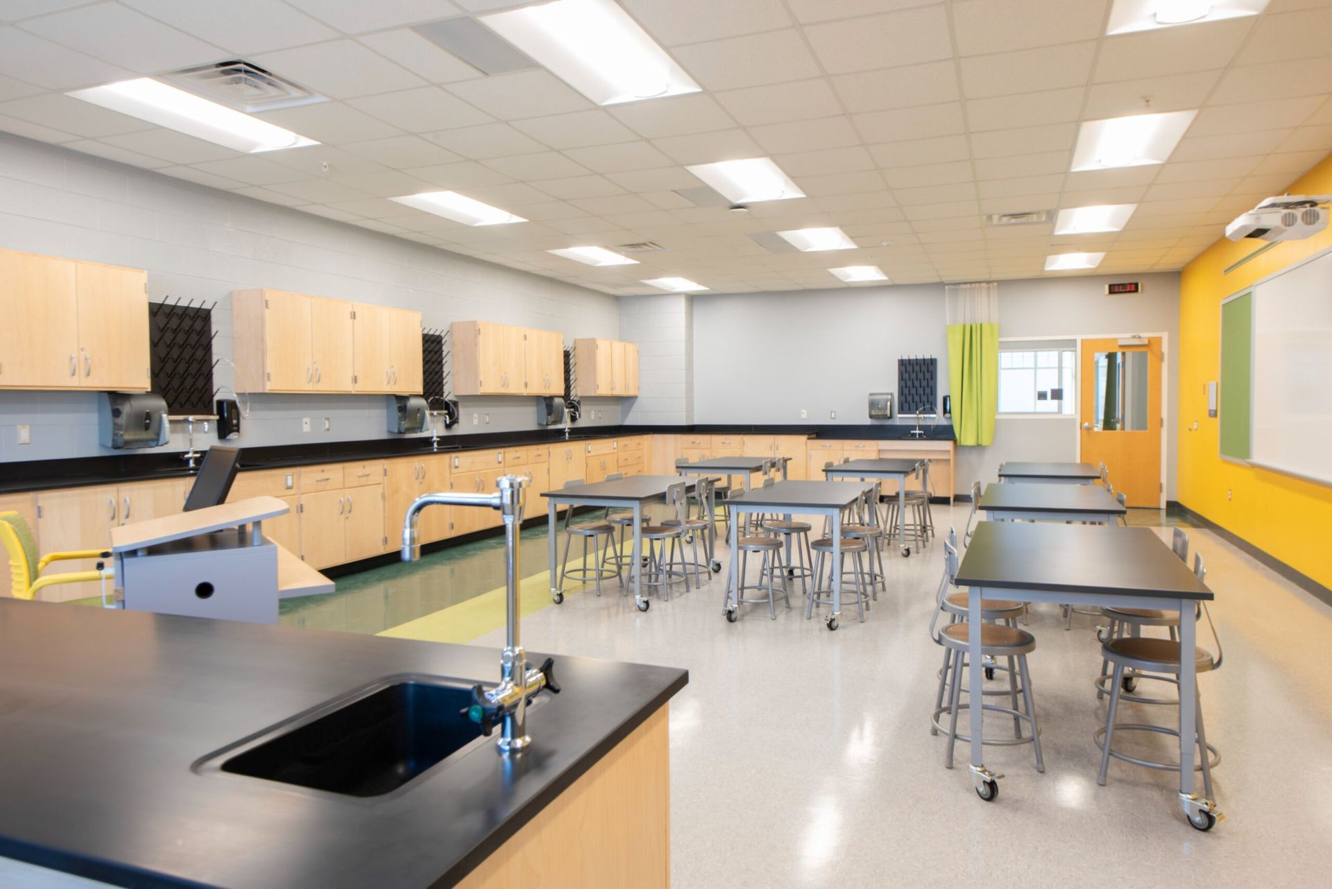 Bright science classroom with lab tables, stools, cabinets, and yellow walls under fluorescent lights