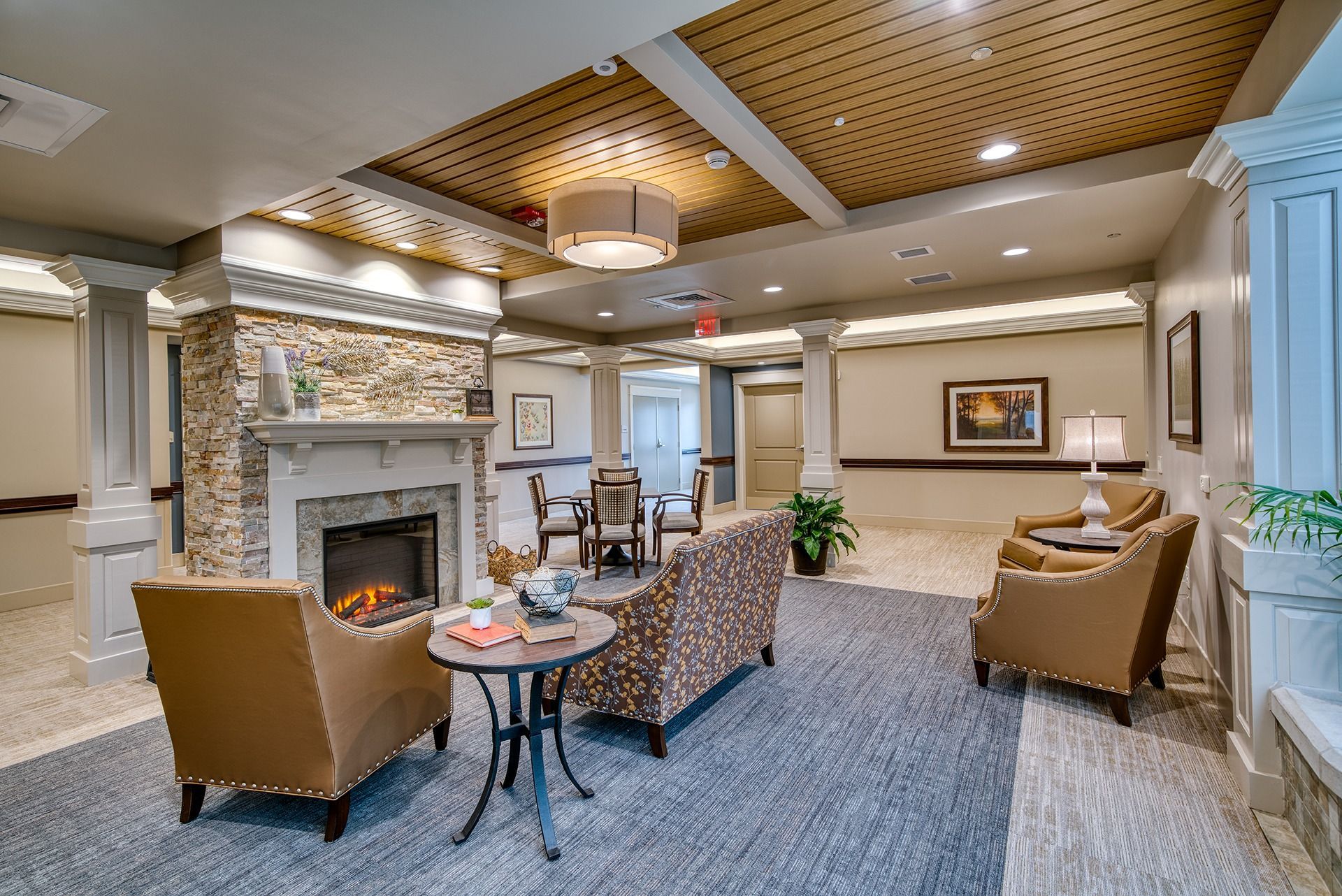 Cozy hotel lobby with fireplace, patterned armchairs, round tables, and warm wood ceiling lights