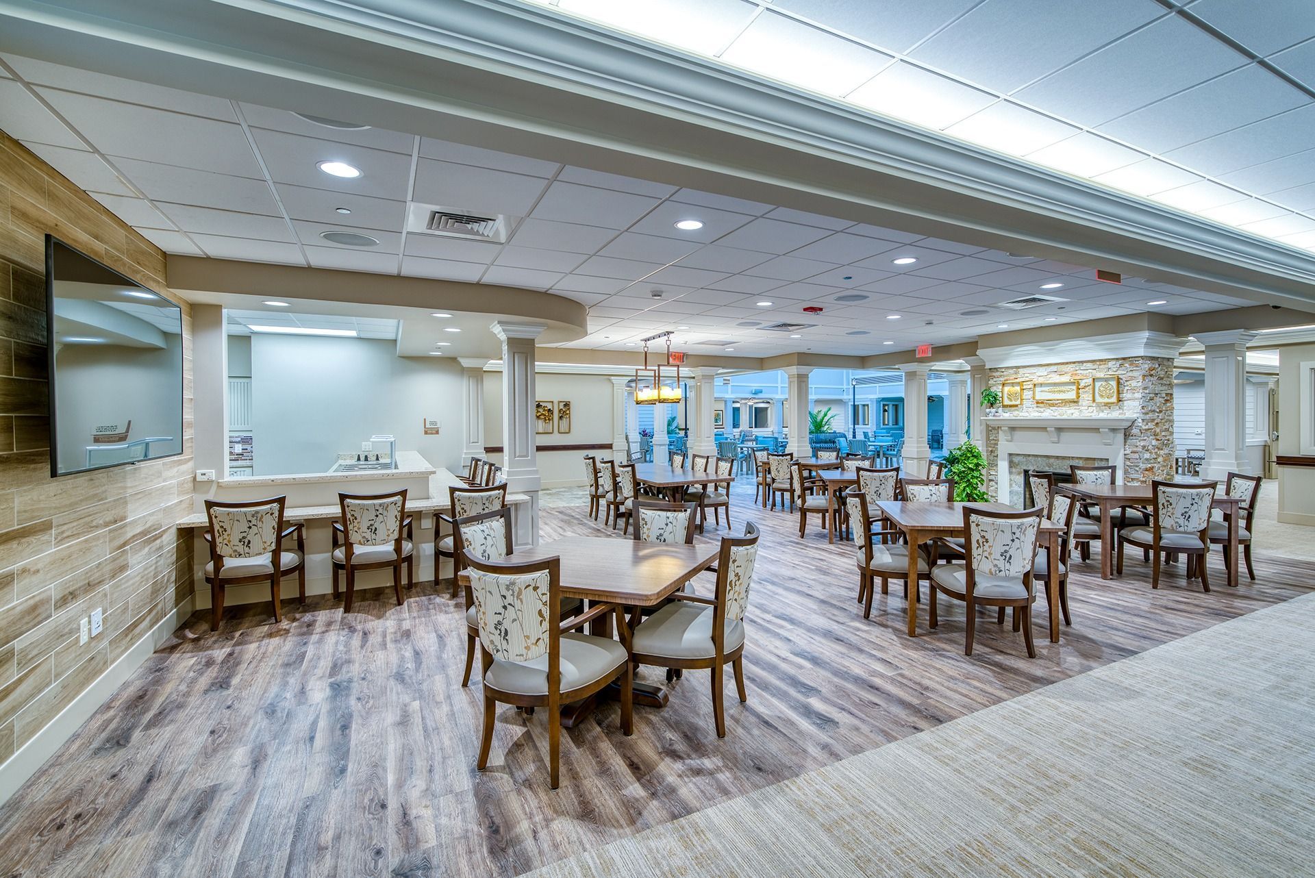 Bright dining room with tables and chairs, wood flooring, and large windows in a modern restaurant.