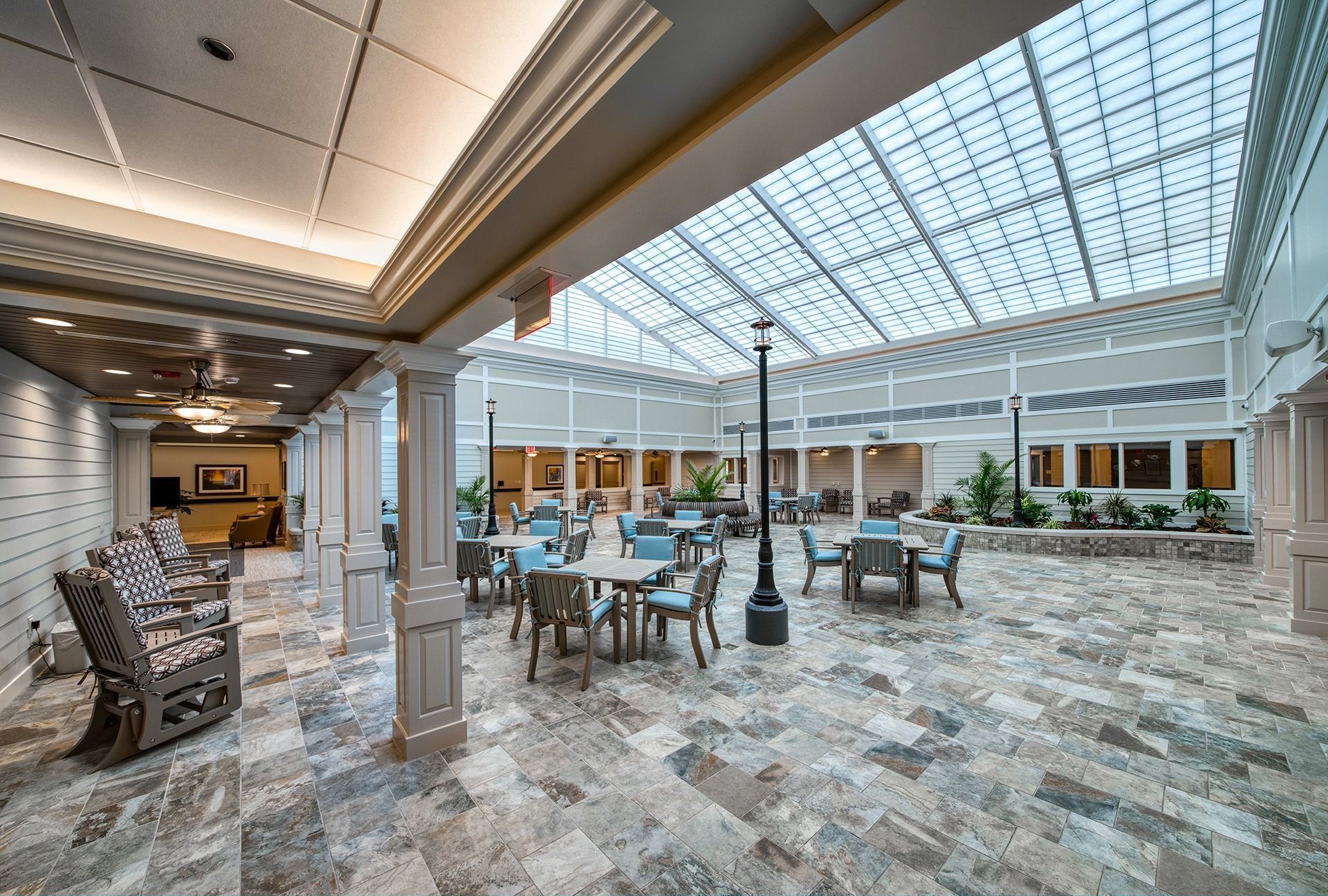 Bright hotel atrium with skylit ceiling, marble floor, and café-style tables and chairs