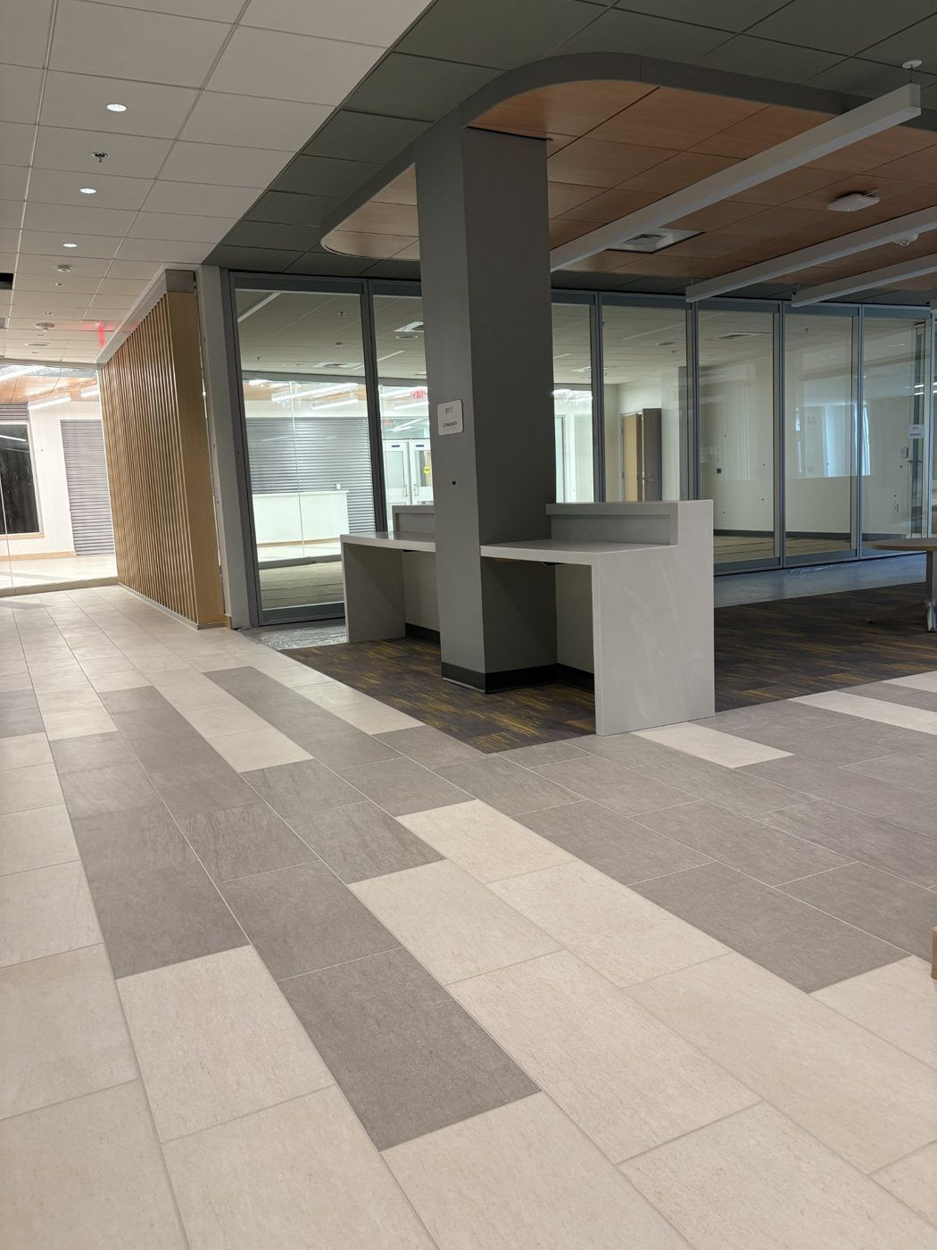 Empty modern indoor lobby with tiled floor, glass walls, and a gray column beside a white podium