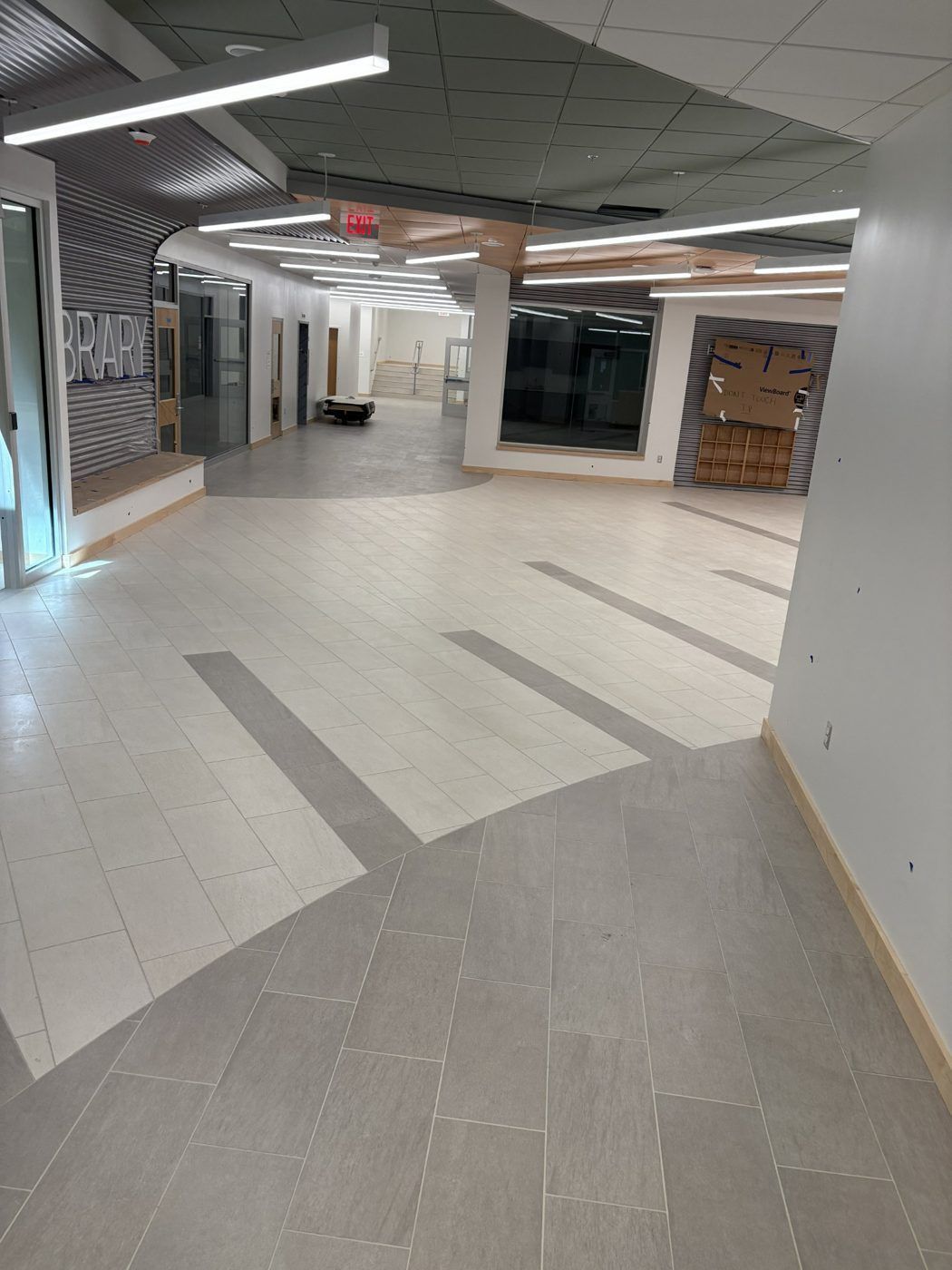 Empty indoor corridor with tiled floor, bright ceiling lights, and storefronts or office entrances along the sides
