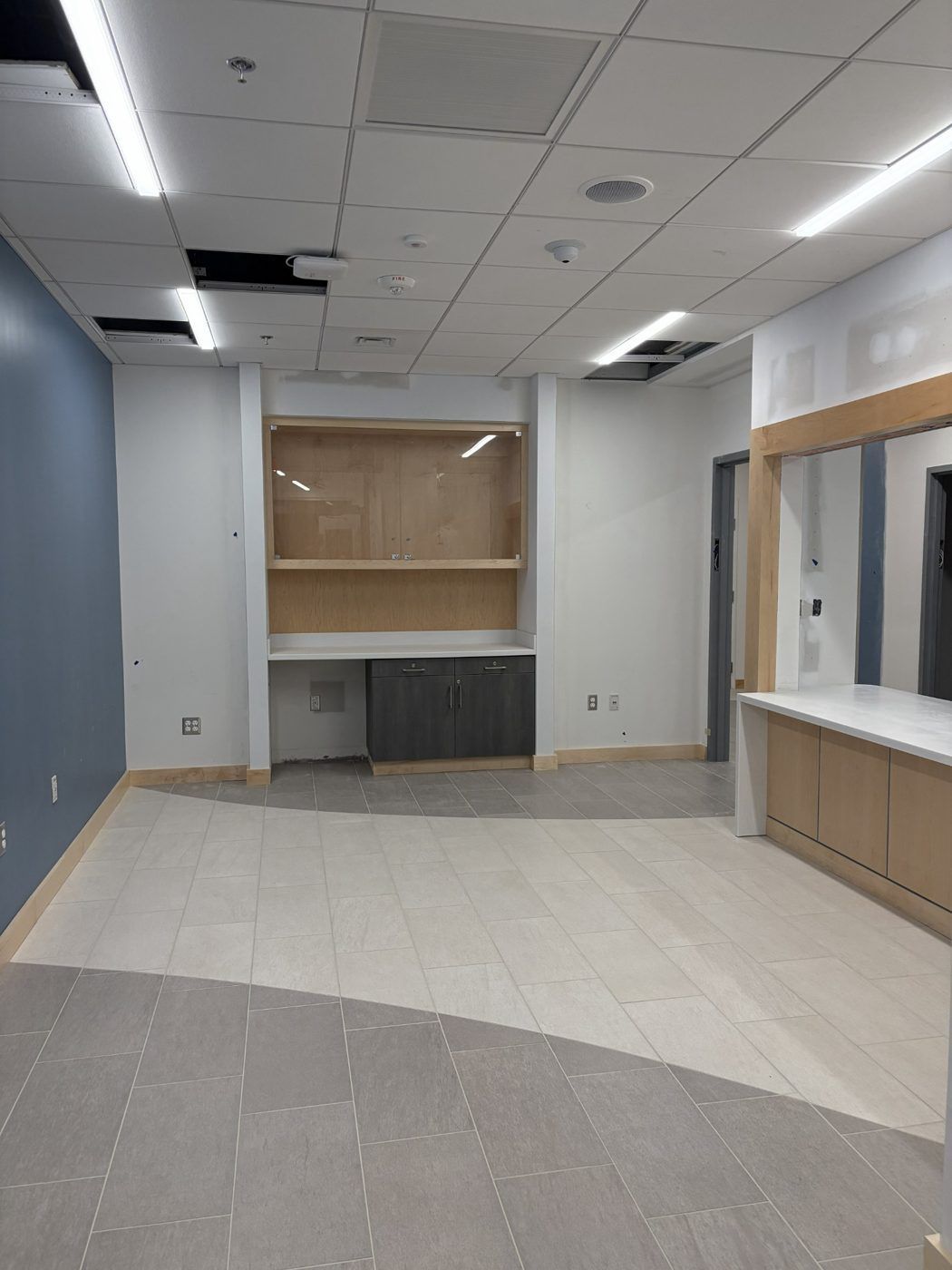 Empty modern interior room with tiled floor, white ceiling lights, and built-in counters along the walls