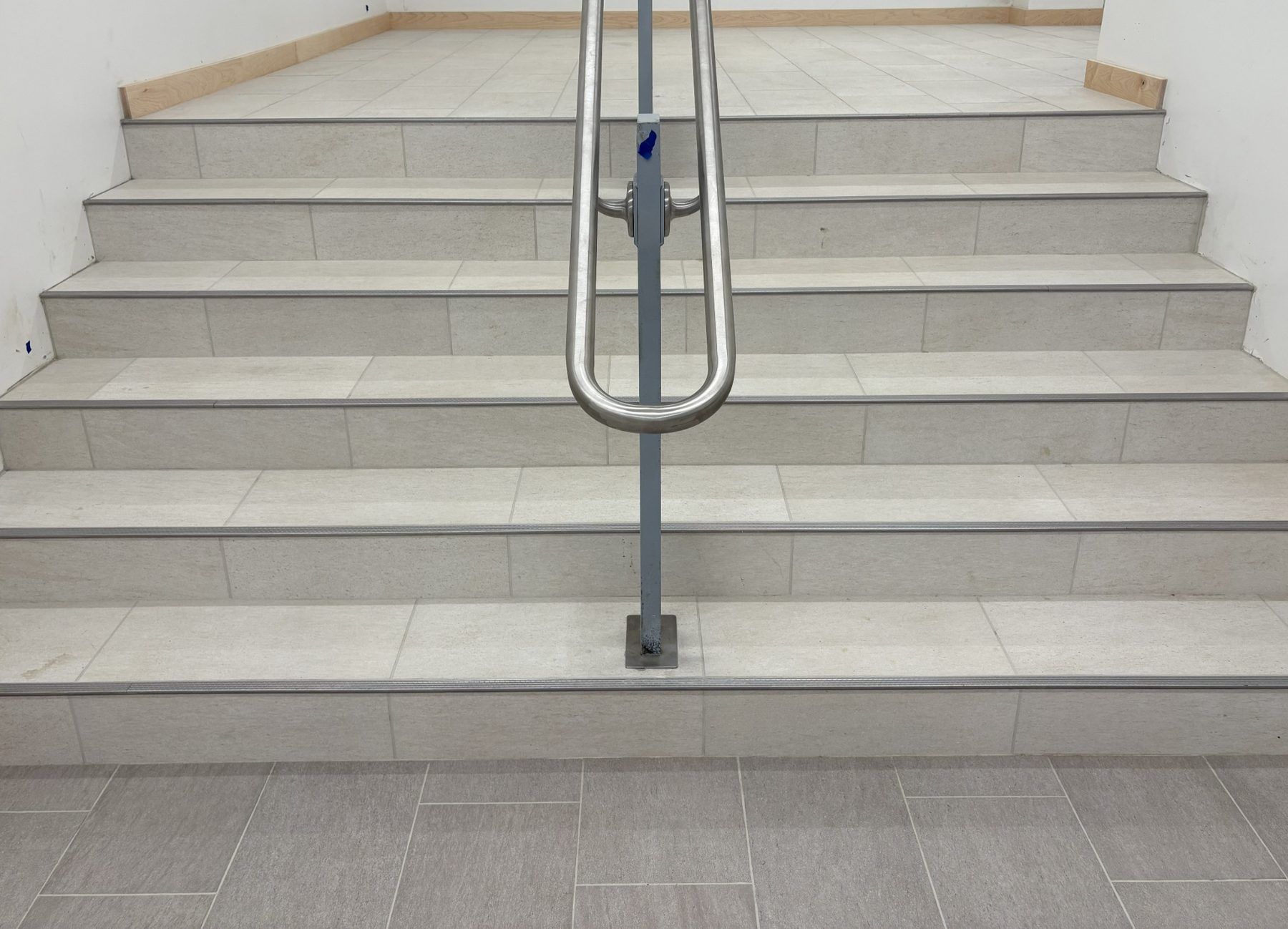 Staircase with metal handrail and beige steps in a tiled indoor area.