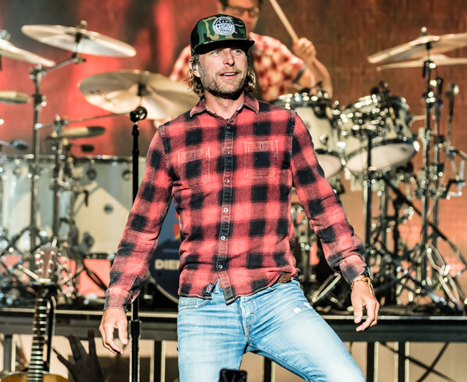 Musician in red plaid shirt and jeans standing on stage with drum kit behind him