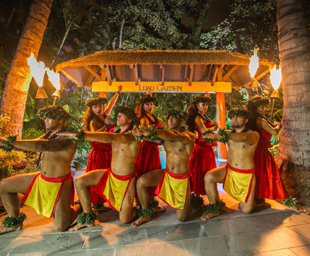 Traditional dancers in red and yellow costumes performing with torches before a lit tropical archway