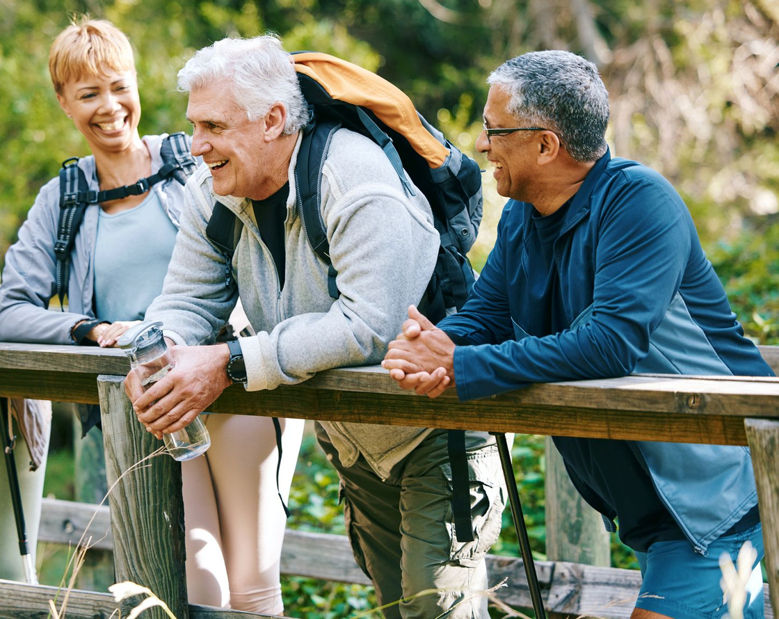 Four people leaning on a wooden fence and chatting outdoors on a sunny day