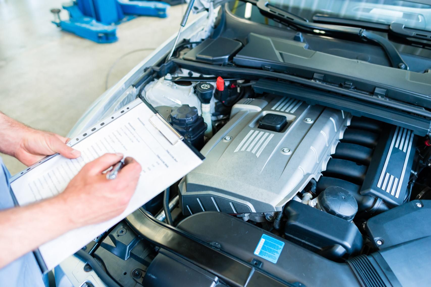 A Man is Looking Under the Hood of a Car While Writing on a Clipboard — Land Rover Spares In Mackay, QLD