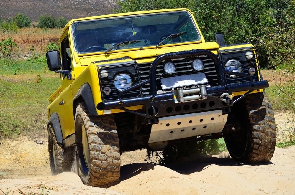 A Yellow Jeep is Driving Down a Dirt Road — Land Rover Spares In Mackay, QLD
