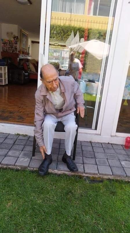 Un anciano está sentado en una silla frente a una puerta corrediza de vidrio.