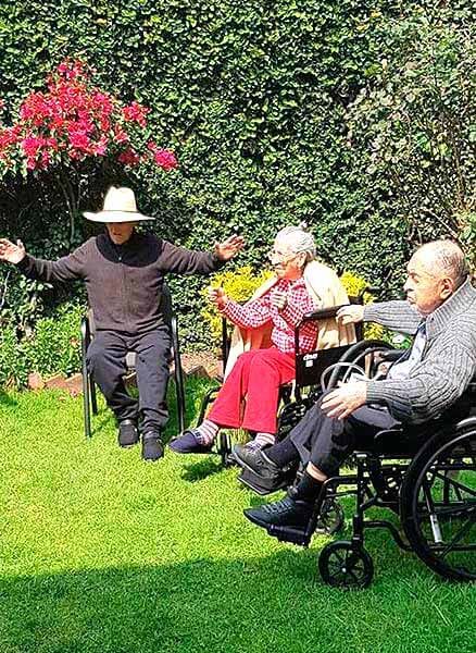 Un grupo de personas mayores están sentadas en sillas y sillas de ruedas en un jardín.