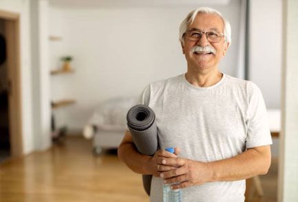 Un anciano sostiene una esterilla de yoga y una botella de agua.