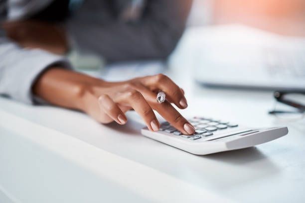 A woman is using a calculator on a desk.