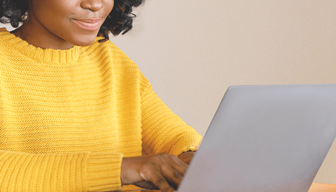 A woman in a yellow sweater is using a laptop computer.