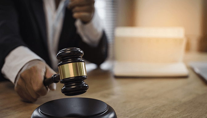 A judge is holding a gavel in his hand while sitting at a table.