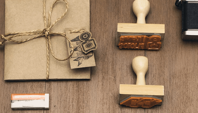 Three wooden stamps are sitting on a wooden table next to a brown envelope.