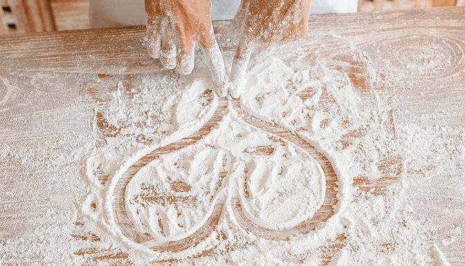 A person is drawing a heart in flour on a wooden table.