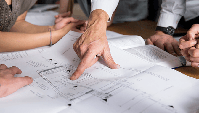 A group of people are sitting around a table looking at a blueprint.