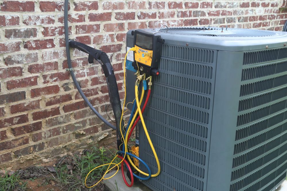 An air conditioner is being serviced by a plumber in front of a brick wall.